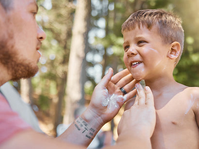 Dad applying sun cream to his sons face