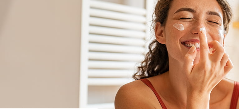 banner of woman smiling as she applies face cream for multi-purpose skin care category